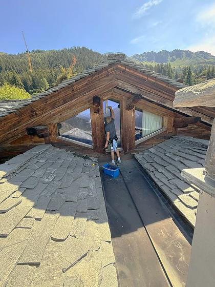 Cleaning a dormer window on a stone-tiled chalet roof above Verbier.